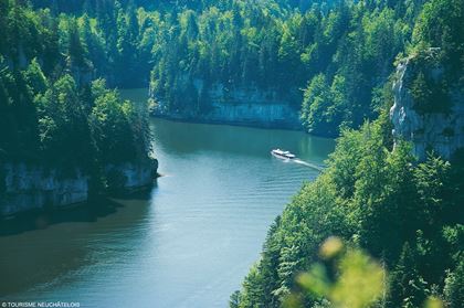 Ein Boot unterwegs auf dem Doubs in einer imposanten Landschaft aus schroffen Felswänden und Tannenwäldern.