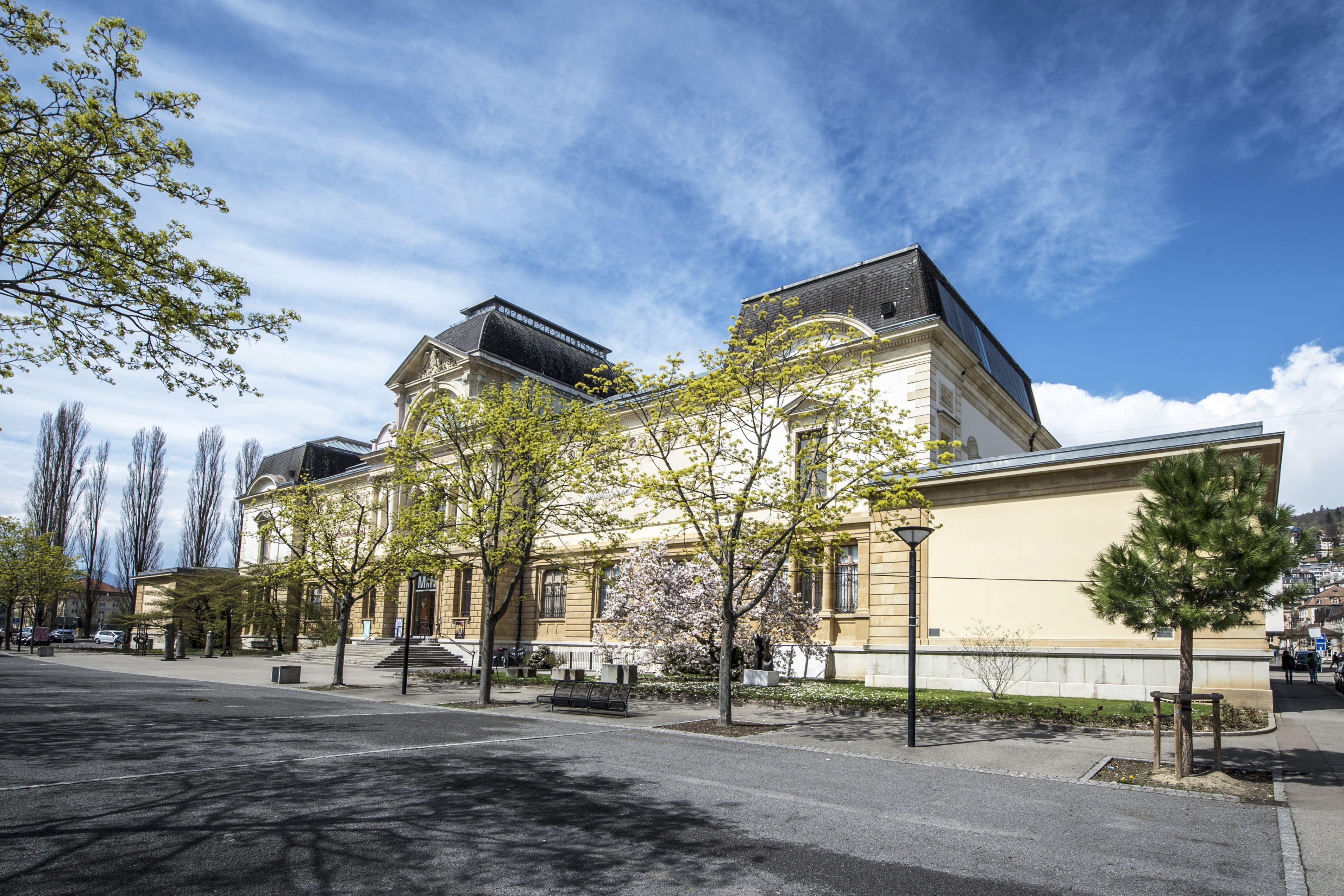 Aussenansicht des Museums für Geschichte und Kunst in Neuenburg. Im Vordergrund stehen Bäume und eine Sitzbank.