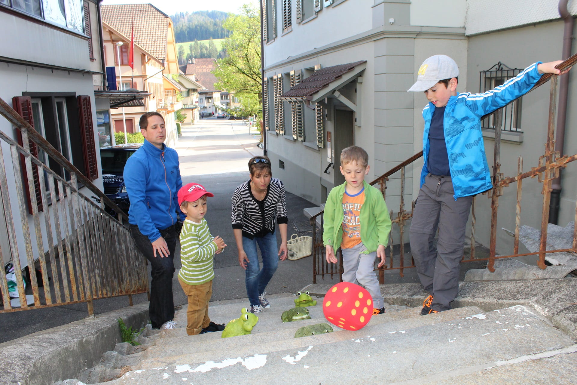 Langnau Tourismus - Spiel dich durch Langnau: Familie beim Spiel mit einem Schaumstoffwürfel und Spielfröschen auf einer Treppe im Freien.