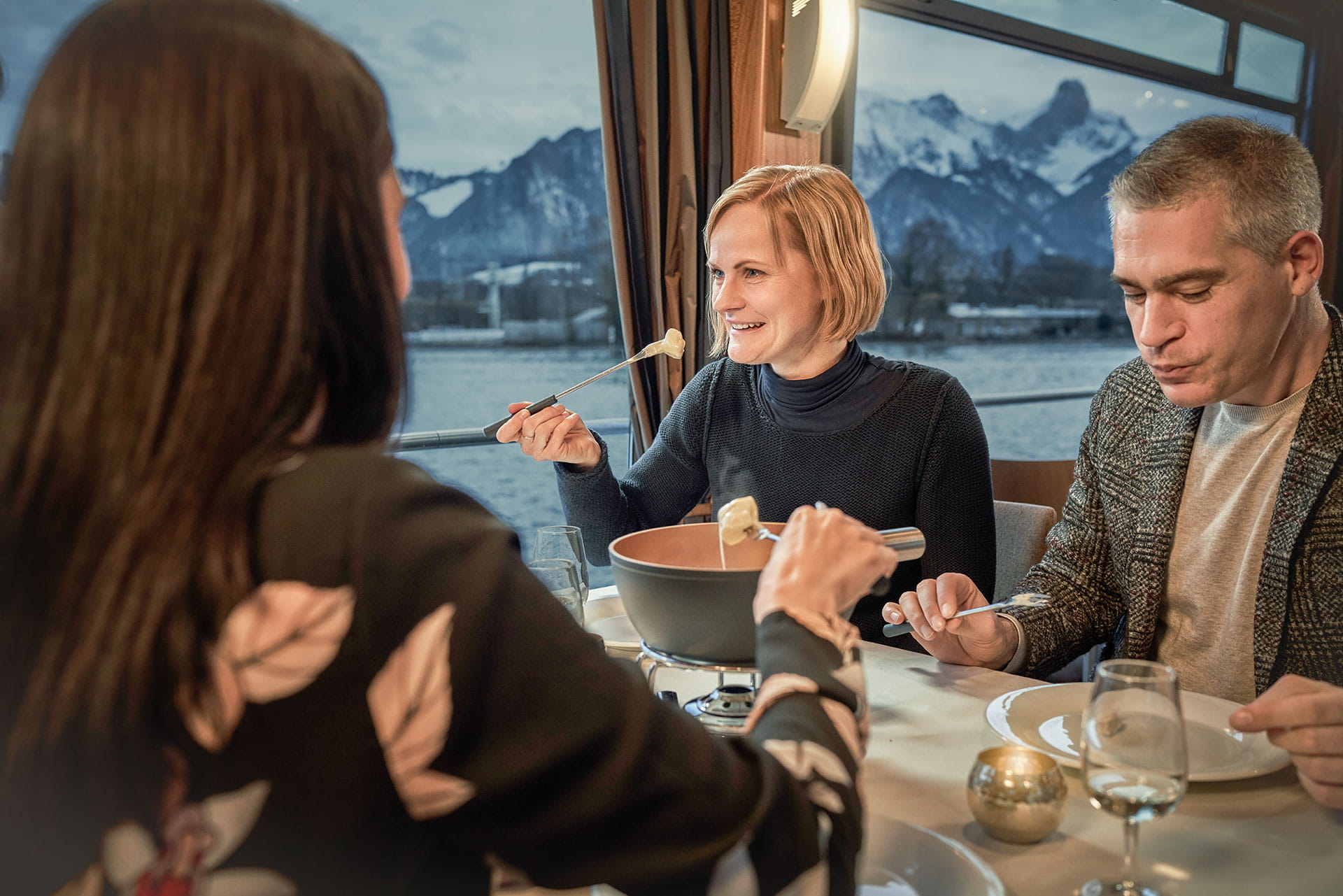 Several people sitting on laid table for Swiss cheese Fondue on the boat